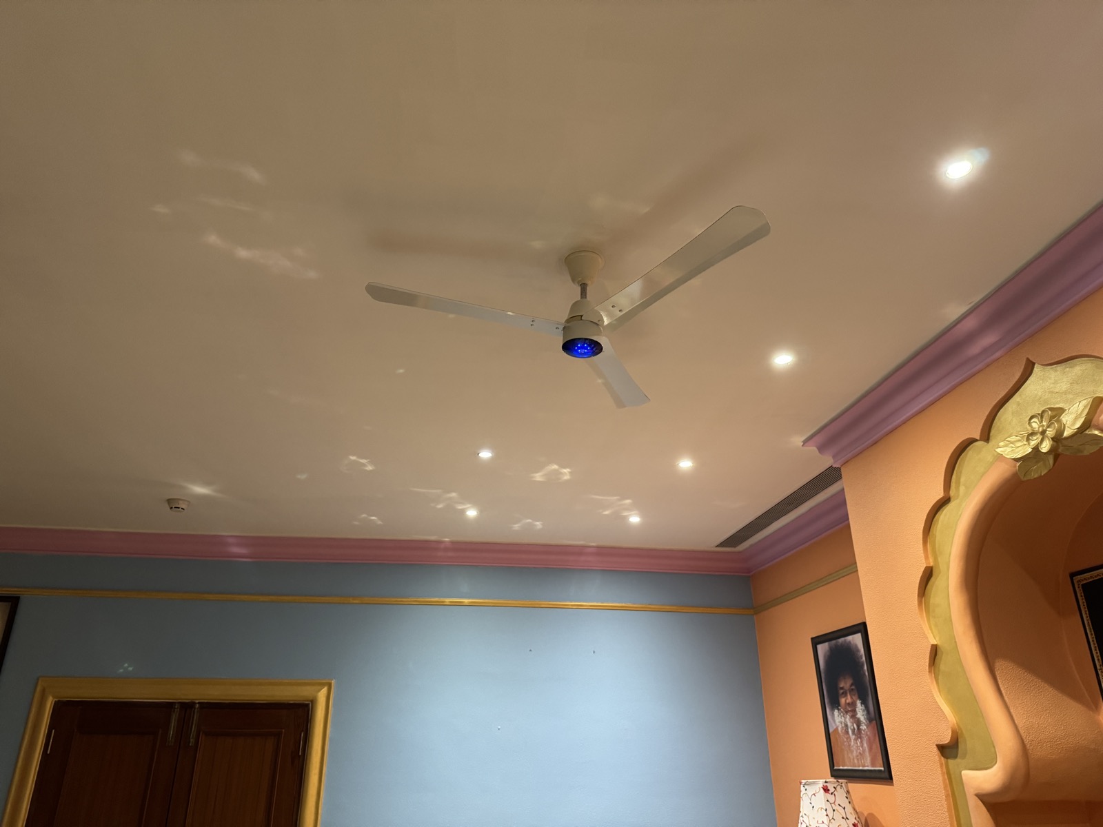 A white BLDC ceiling fan with a blue indicator light, installed in a campus room